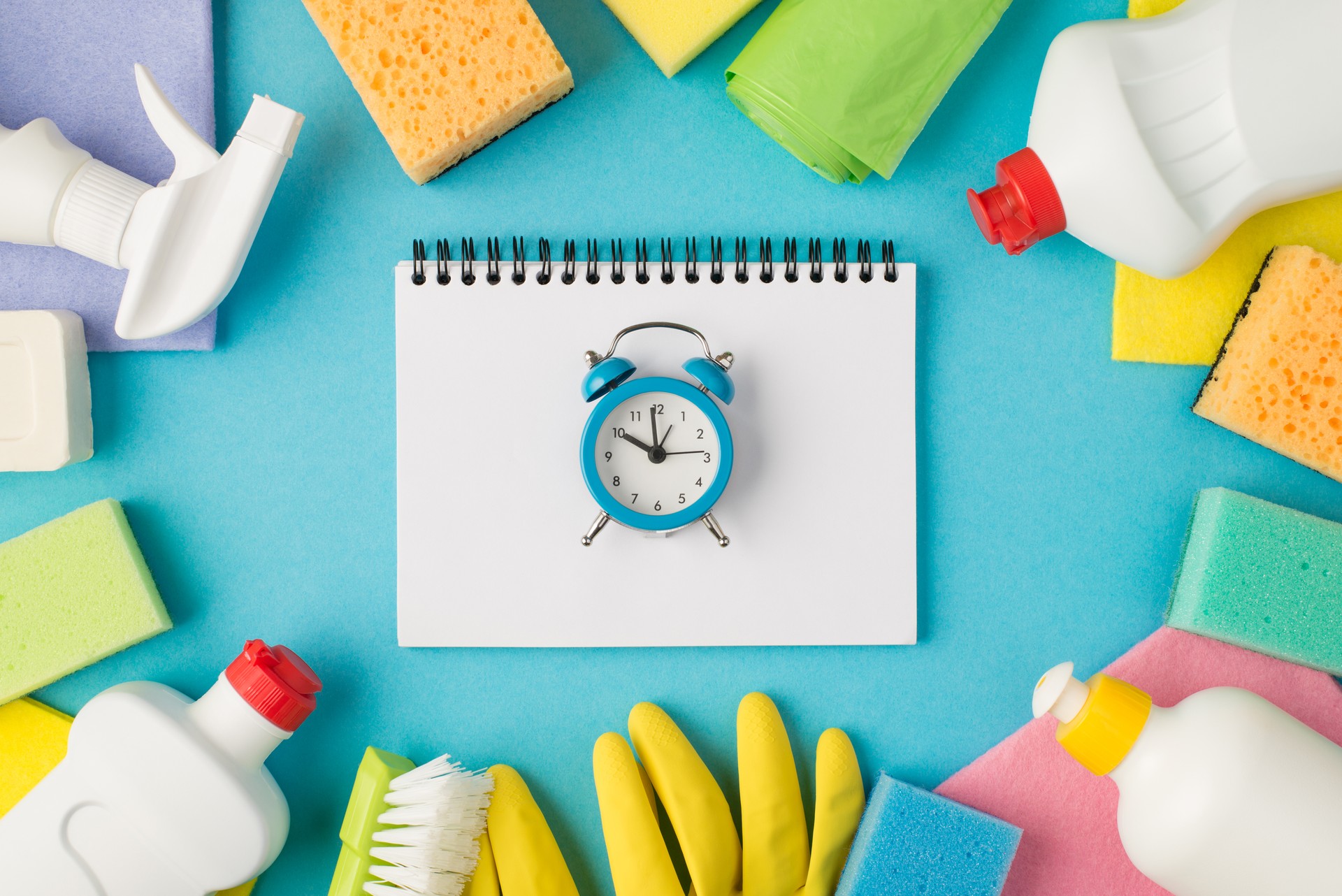 Above photo of equipment for cleaning and notebook with alarm clock in the middle isolated on the blue background